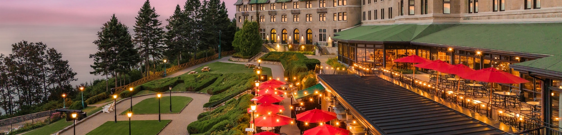 dining area with red umbrellas lit up with string lights at sunset
