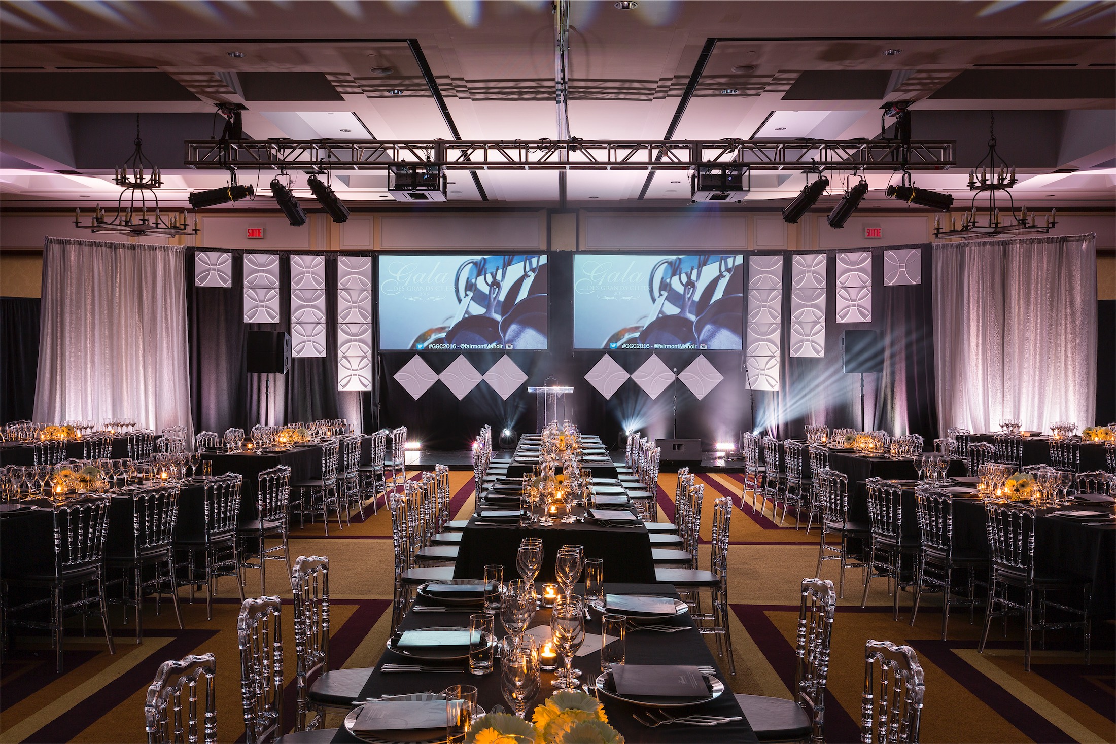 large meeting room set up with rectangle tables and plastic chairs with a podium for a speaker
